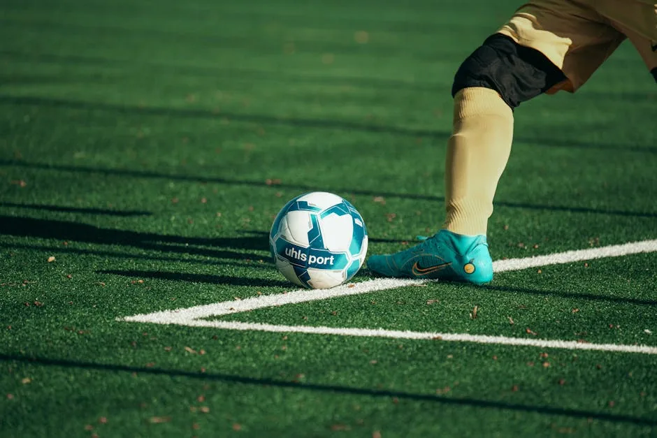 Close-up of a football player preparing to kick a blue and white soccer ball on a turf field.