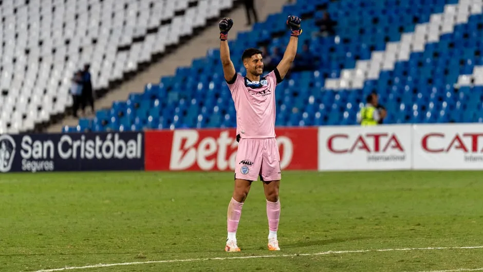 Footballer in pink uniform celebrating a victory in an empty stadium.